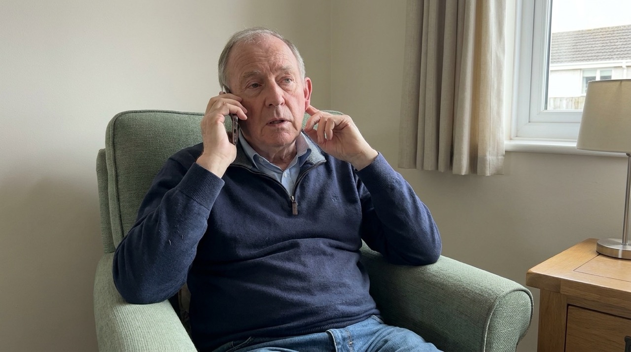 Older man struggling to follow a phone conversation while seated at home.